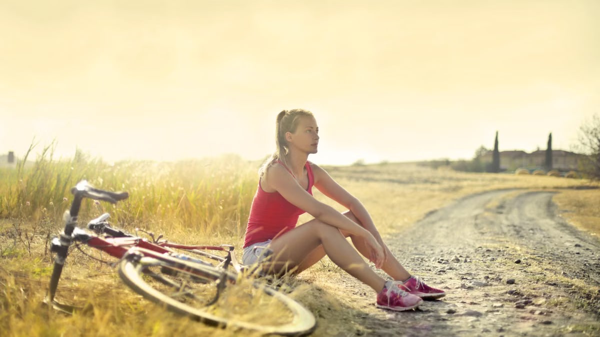 Woman sitting thoughtfully by her bicycle on a rural dirt road.
